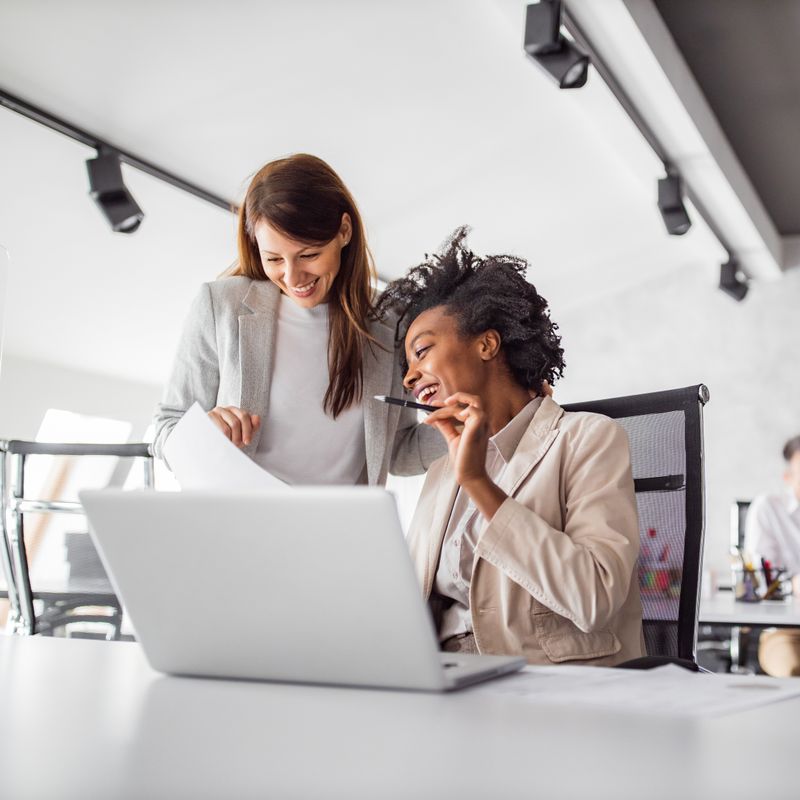 Two women working on a laptop in a bright, well-lit design studio.