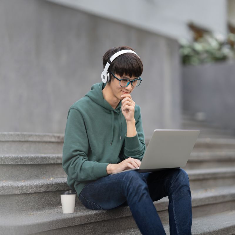 A boy sitting on some stone steps, looking at a laptop screen.